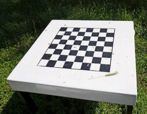 weißer, quadratischer Tisch mit aufgemaltem Schachbrett auf einer Wiese stehend