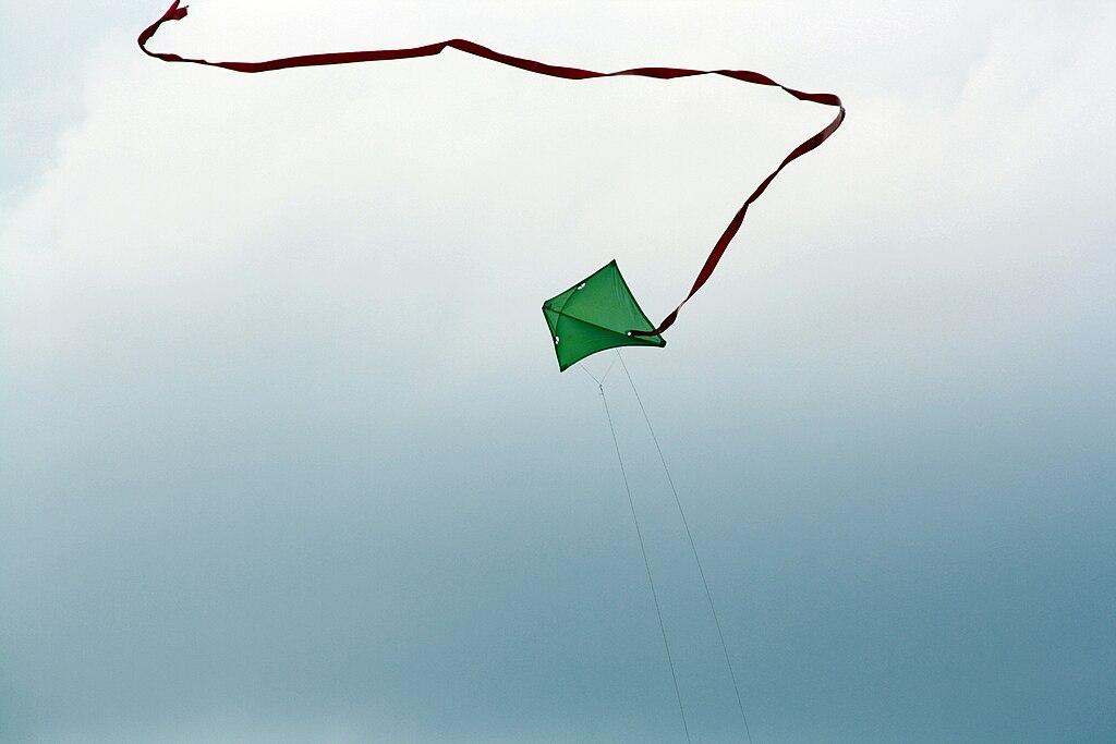 Grüner Trapezdrache mit langer rotbrauner Schnur in den Himmel steigend