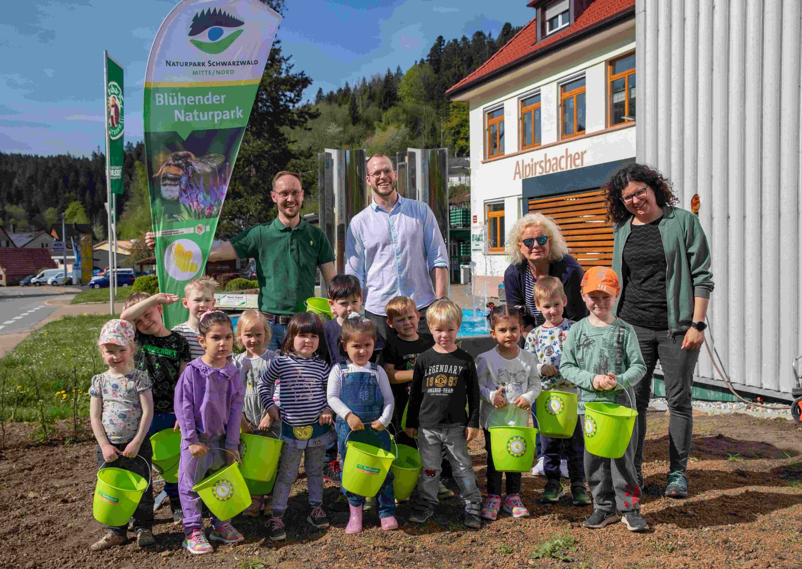 Gruppenfoto von Kindern mit grünen Eimern bei der Einsaat einer Wildblumenwiese.