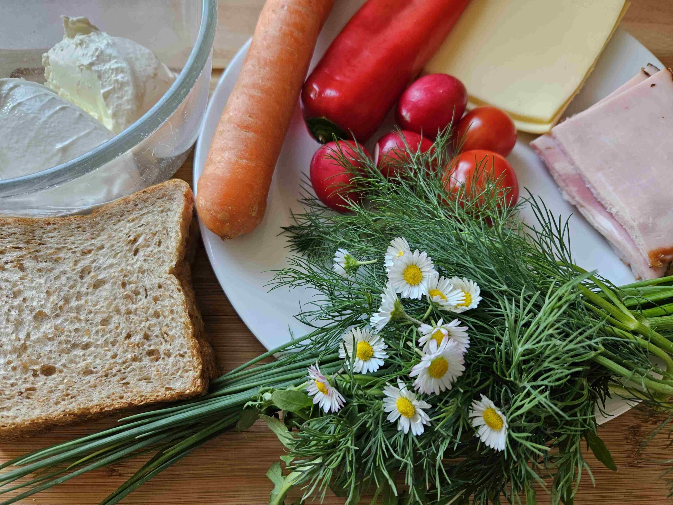 Zutaten für das Wiesen-Sandwich: Kräuter, Vollkorntoast, Frischkäse, Schinken, Käse, Paprika, Karotte, Tomaten, Radieschen, Gänseblümchen