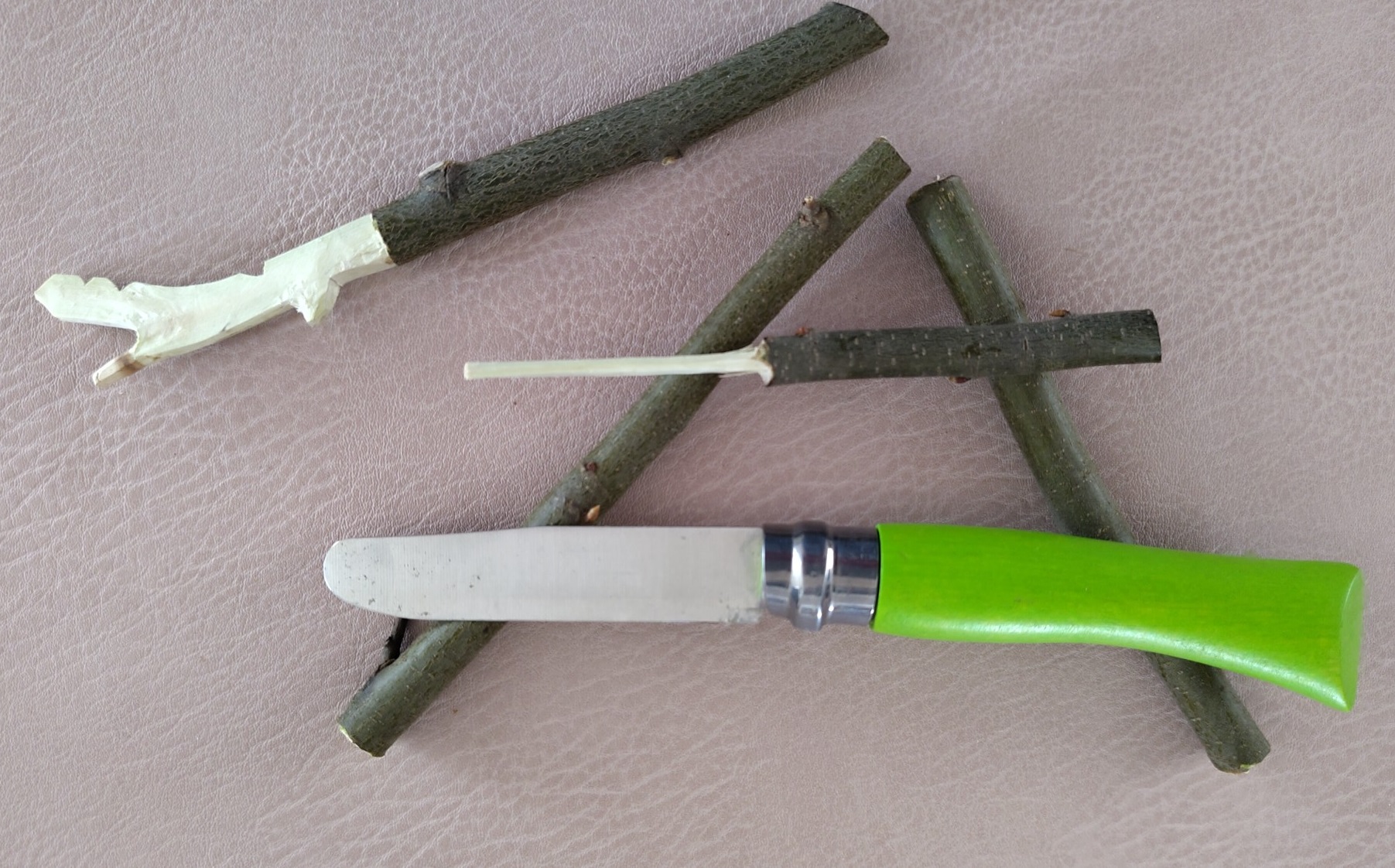 Anordnung von 4 teilweise geschnitzten Hölzchen mit Rinde und einem grünen Kindertaschenmesser